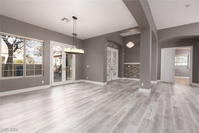 unfurnished dining area featuring french doors, light wood-type flooring, and an inviting chandelier