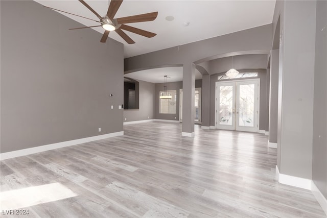 unfurnished living room with ceiling fan with notable chandelier, light wood-type flooring, and french doors