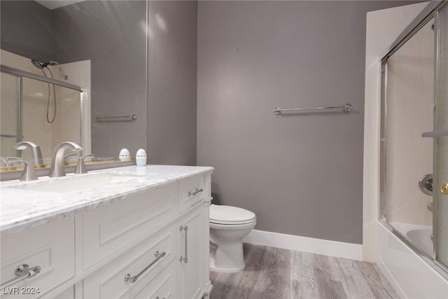 full bathroom with shower / bath combination with glass door, hardwood / wood-style floors, vanity, and toilet