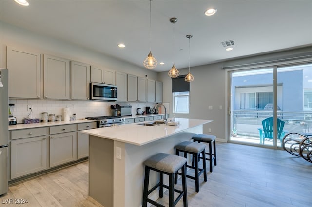 kitchen featuring pendant lighting, a kitchen island with sink, sink, decorative backsplash, and appliances with stainless steel finishes