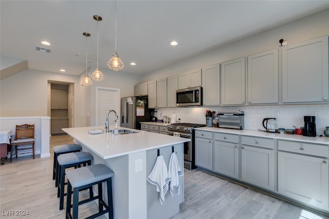 kitchen with appliances with stainless steel finishes, decorative light fixtures, light hardwood / wood-style flooring, and an island with sink