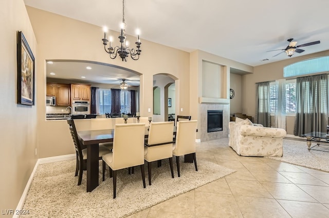 tiled dining area with a fireplace and ceiling fan with notable chandelier