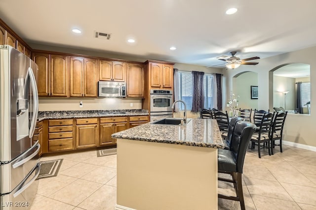 kitchen featuring appliances with stainless steel finishes, a kitchen breakfast bar, dark stone counters, a kitchen island with sink, and sink