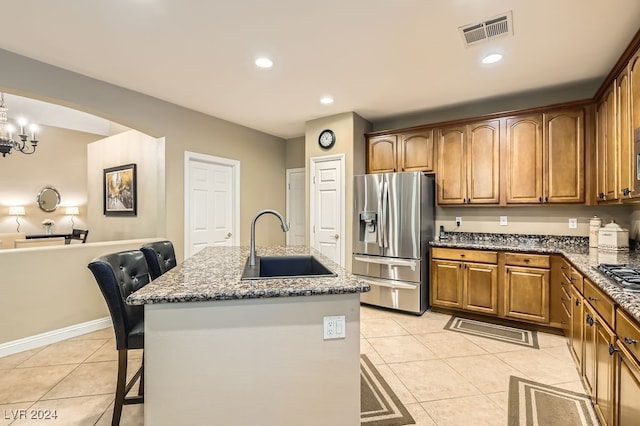 kitchen featuring a kitchen breakfast bar, sink, dark stone countertops, stainless steel fridge with ice dispenser, and an island with sink