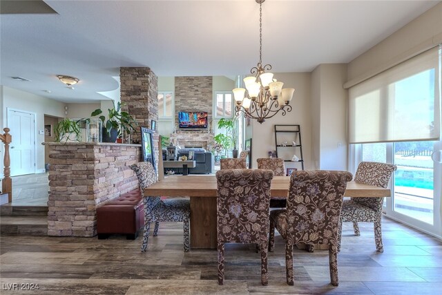 dining room featuring hardwood / wood-style flooring, a stone fireplace, and a notable chandelier