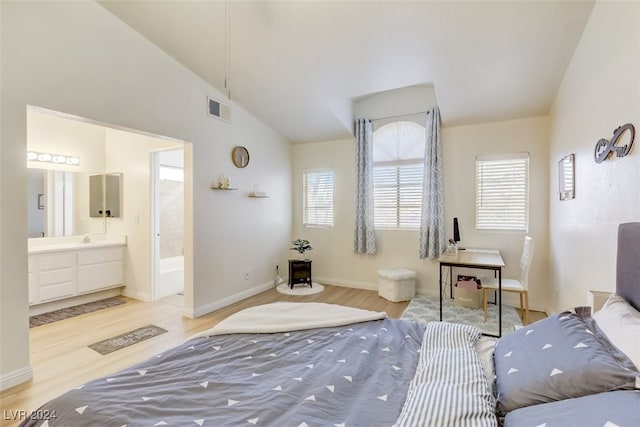 bedroom featuring light wood-type flooring, ensuite bathroom, and lofted ceiling