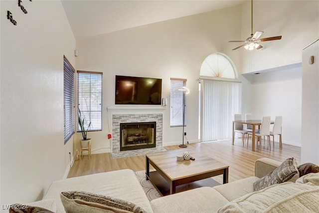 living room with a stone fireplace, ceiling fan, high vaulted ceiling, and light wood-type flooring