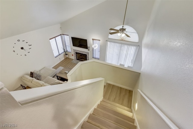 staircase featuring ceiling fan, wood-type flooring, high vaulted ceiling, and a brick fireplace