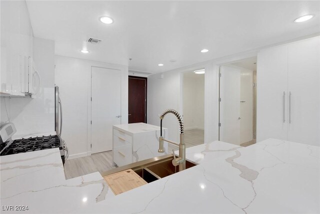 4575 Dean Martin Dr Unit 2211, Las Vegas, NV 89103 - kitchen with gas stove, light wood-type flooring, recessed lighting, white cabinets, and light stone countertops