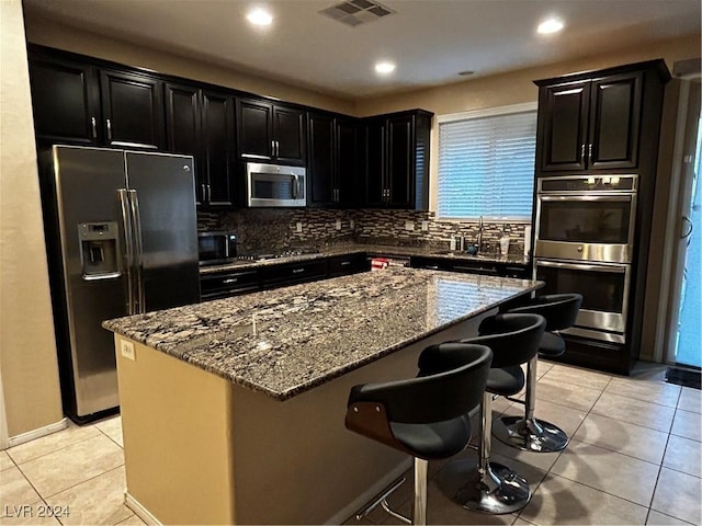 kitchen featuring stone counters, stainless steel appliances, light tile patterned floors, a breakfast bar area, and a kitchen island