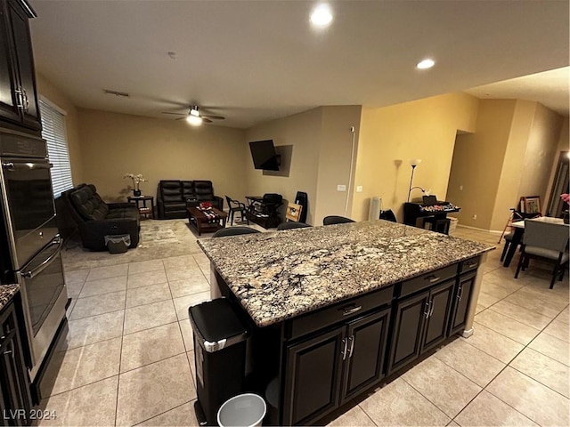 kitchen with ceiling fan, light stone countertops, light tile patterned floors, double oven, and a kitchen island