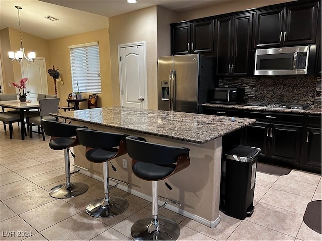 kitchen featuring a kitchen bar, stainless steel appliances, a notable chandelier, a center island, and light tile patterned flooring