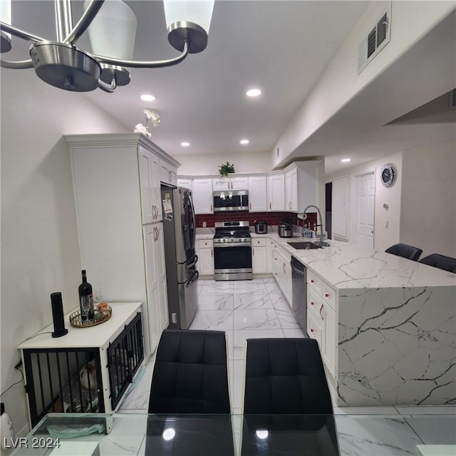 kitchen with sink, decorative backsplash, light stone countertops, appliances with stainless steel finishes, and white cabinetry