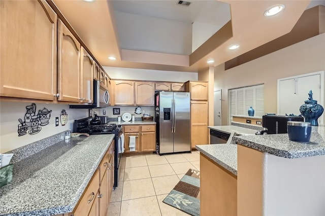 kitchen with light stone counters, a tray ceiling, light brown cabinetry, light tile patterned flooring, and appliances with stainless steel finishes