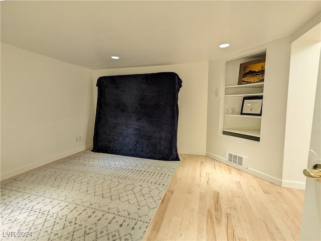 empty room with built in shelves and wood-type flooring