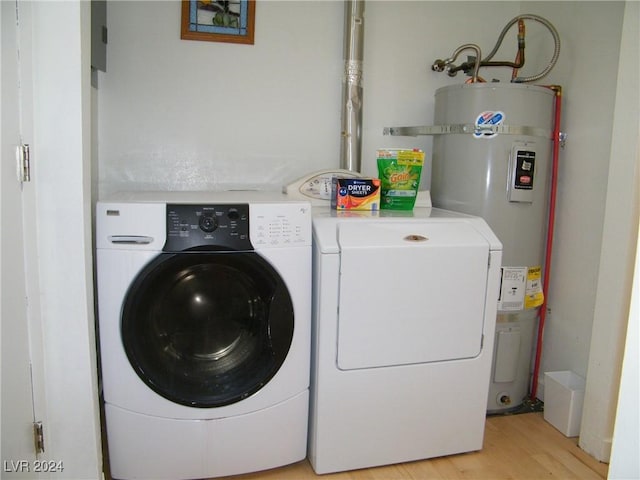 laundry area featuring strapped water heater, washing machine and clothes dryer, and light wood-style flooring