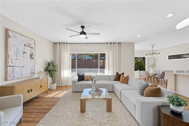 living room with ceiling fan with notable chandelier and hardwood / wood-style flooring