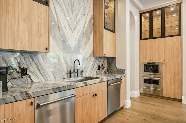 kitchen with stone counters, sink, stainless steel appliances, backsplash, and light wood-type flooring