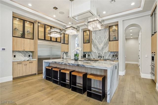 kitchen featuring tasteful backsplash, light stone counters, stainless steel appliances, pendant lighting, and light hardwood / wood-style floors