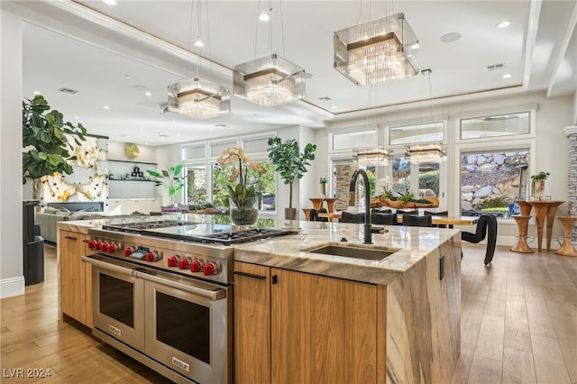 kitchen featuring range with two ovens, sink, an island with sink, light hardwood / wood-style floors, and light stone counters