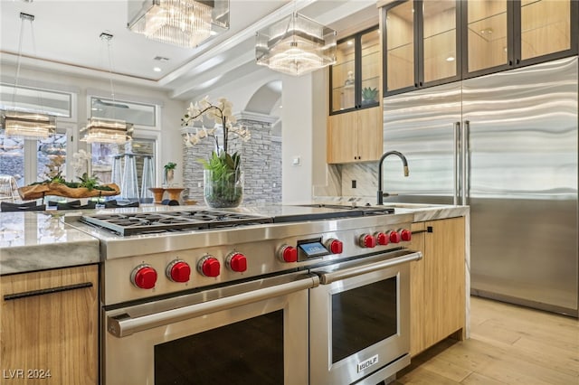 kitchen with hanging light fixtures, a notable chandelier, high quality appliances, light hardwood / wood-style floors, and decorative backsplash