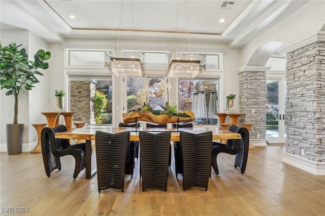 dining area featuring light wood-type flooring, a tray ceiling, and ornate columns