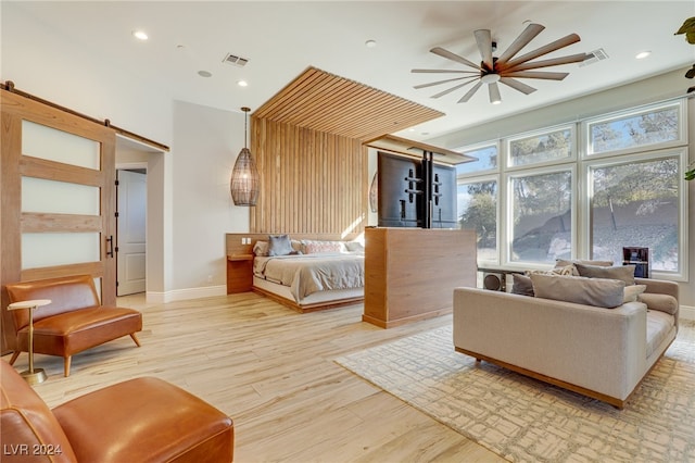 bedroom featuring a barn door, ceiling fan, and light wood-type flooring