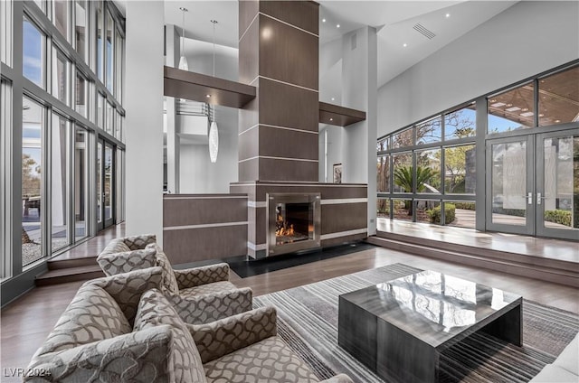 living room with a high ceiling, a large fireplace, french doors, and dark wood-type flooring