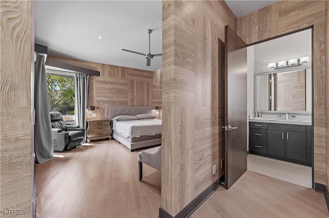 bedroom with wood walls, ensuite bathroom, light hardwood / wood-style floors, and sink