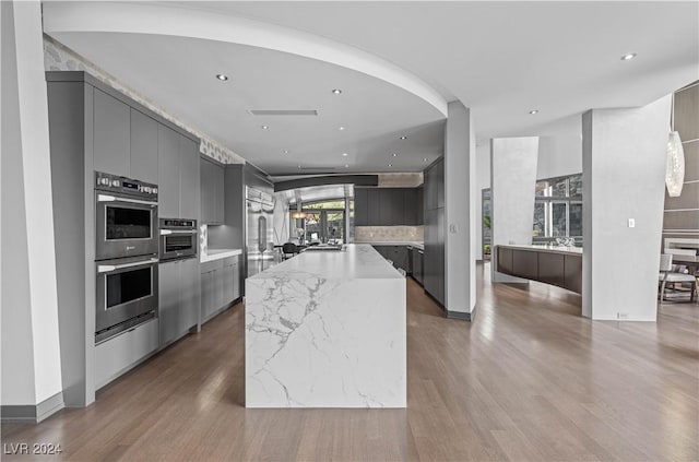 kitchen with a kitchen island, stainless steel double oven, wood-type flooring, and light stone counters