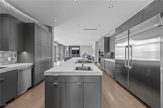 kitchen with stainless steel appliances, tasteful backsplash, light hardwood / wood-style flooring, an island with sink, and gray cabinets