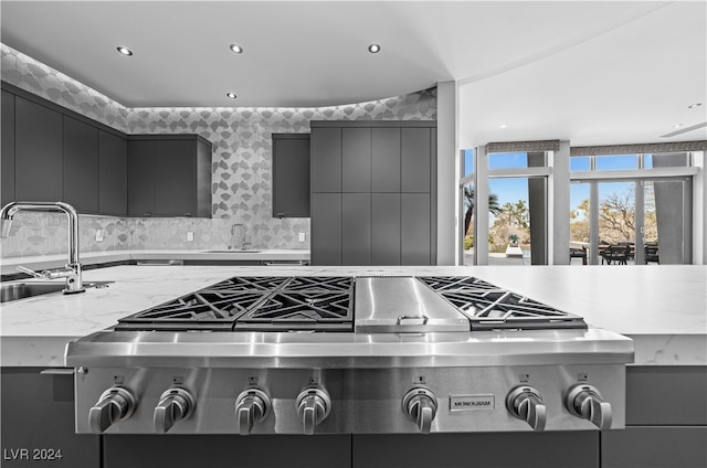 kitchen with tasteful backsplash, light stone countertops, sink, and stainless steel gas stovetop