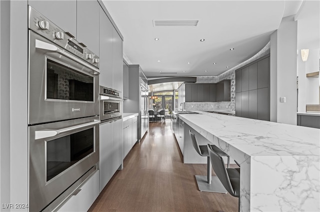 kitchen featuring gray cabinetry, sink, dark hardwood / wood-style floors, light stone counters, and stainless steel double oven