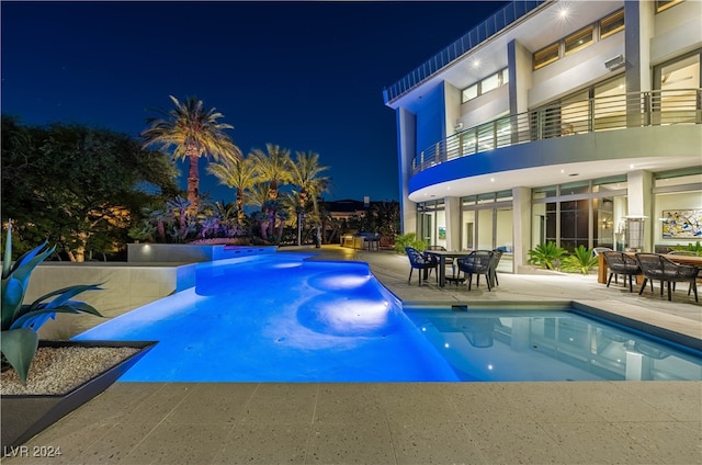 pool at night featuring a patio area