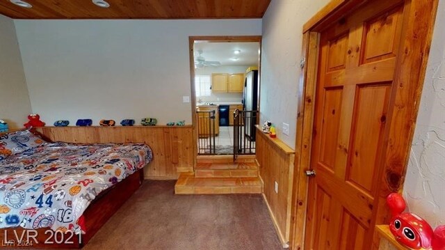 carpeted bedroom featuring wood ceiling, wooden walls, and stainless steel fridge