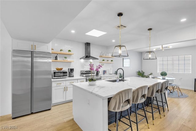 kitchen with white cabinets, a center island with sink, wall chimney exhaust hood, and stainless steel appliances