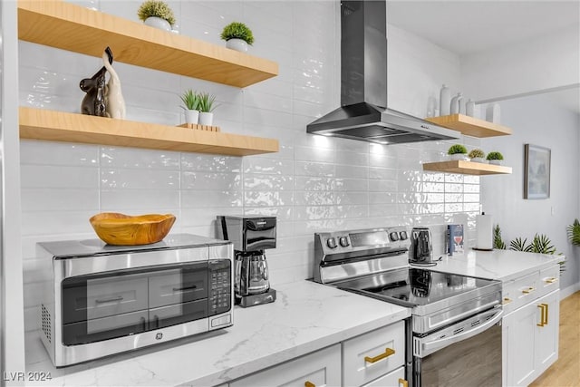 kitchen with light stone counters, wall chimney exhaust hood, stainless steel appliances, light hardwood / wood-style flooring, and white cabinetry