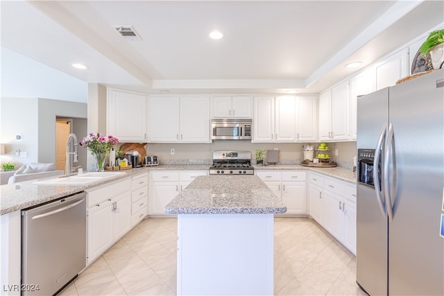 kitchen featuring light stone counters, stainless steel appliances, sink, white cabinetry, and a kitchen island