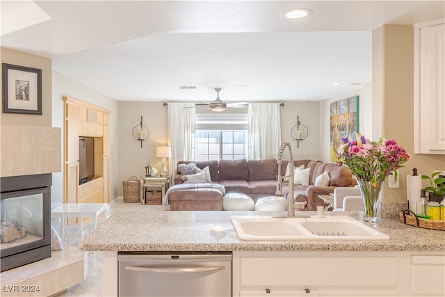 kitchen featuring light stone countertops, white cabinets, sink, a tile fireplace, and dishwasher