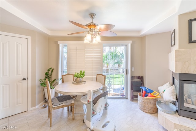 dining area featuring ceiling fan, a tile fireplace, and a tray ceiling