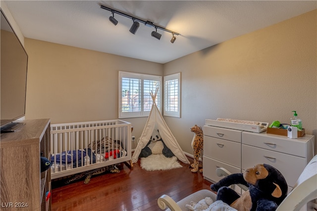 bedroom featuring dark hardwood / wood-style flooring, track lighting, and a crib