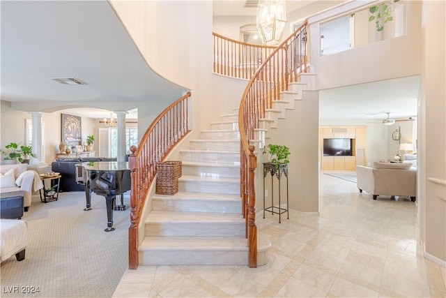 staircase featuring a notable chandelier, ornate columns, and a towering ceiling