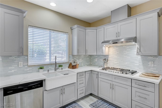 kitchen with gray cabinetry, backsplash, sink, light stone countertops, and appliances with stainless steel finishes