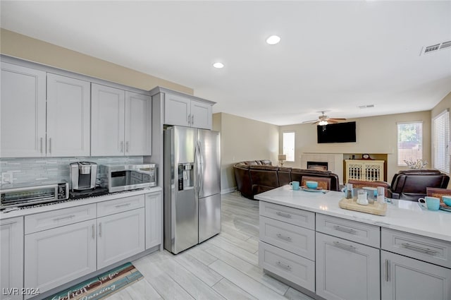 kitchen featuring decorative backsplash, light wood-type flooring, stainless steel appliances, ceiling fan, and a fireplace