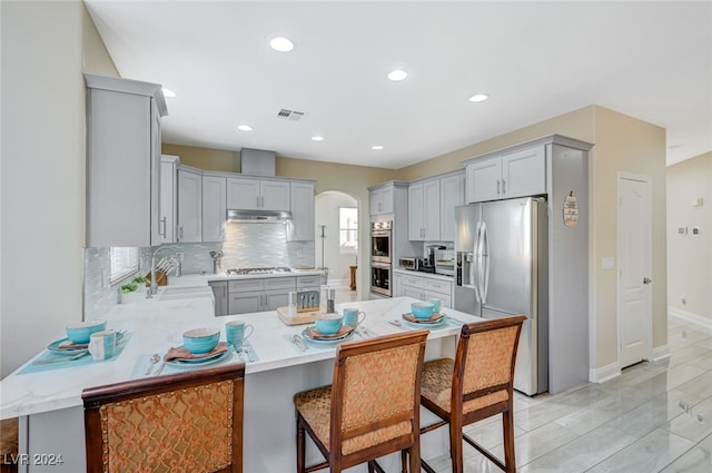 kitchen with decorative backsplash, gray cabinetry, stainless steel appliances, sink, and a breakfast bar area