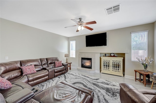 living room with ceiling fan, a tiled fireplace, and light hardwood / wood-style flooring