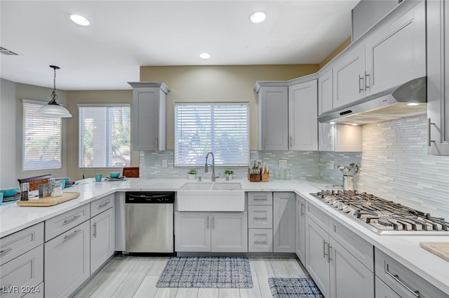 kitchen featuring pendant lighting, gray cabinetry, backsplash, sink, and appliances with stainless steel finishes