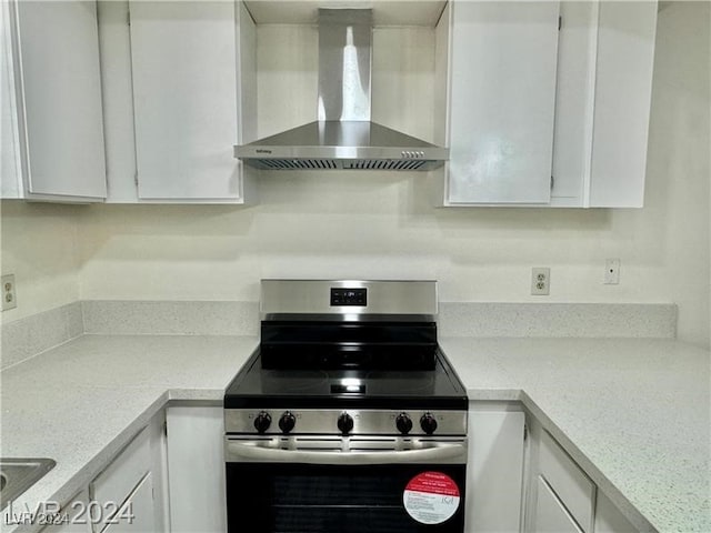 kitchen with stainless steel range, light stone counters, white cabinetry, and wall chimney range hood