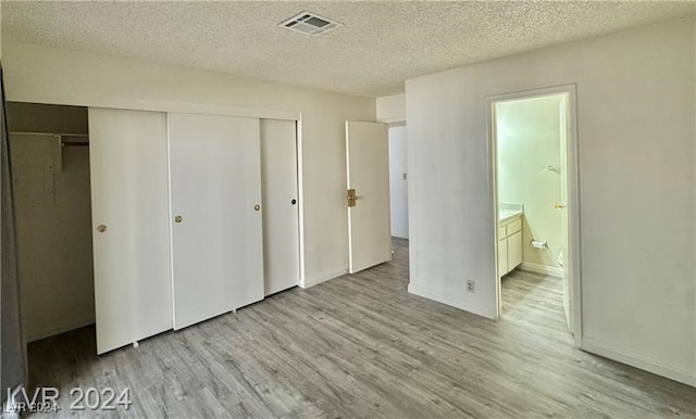 unfurnished bedroom with a closet, a textured ceiling, connected bathroom, and light hardwood / wood-style flooring