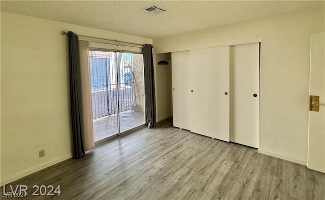 unfurnished bedroom featuring wood-type flooring, a textured ceiling, access to outside, and a closet